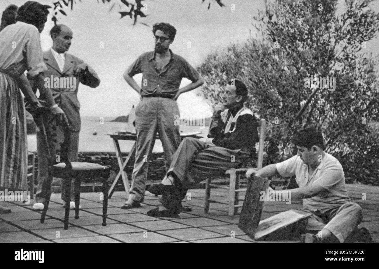 Salvador Dali (1904 - 1989), der surrealistische Künstler, wird abends nach einem Arbeitstag in seinem Sommerhaus in Port Lligat am Fuße der spanischen Pyrenäen gezeigt. Auf der linken Seite steht der katalanische Schriftsteller J. V. Foix. Auf der rechten Seite bereitet sich einer der jungen Schüler des Meisters darauf vor, seine Arbeit zu zeigen. 1951 Stockfoto
