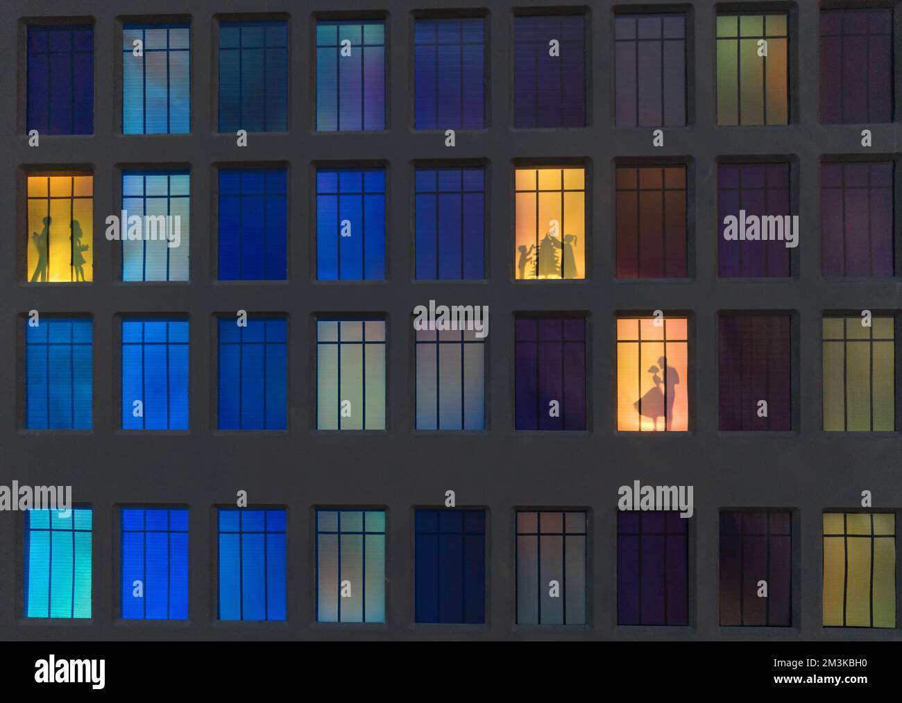 Die Wand eines Nachthauses in den beleuchteten Fenstern, von denen die Silhouetten der Menschen sichtbar sind. Stockfoto