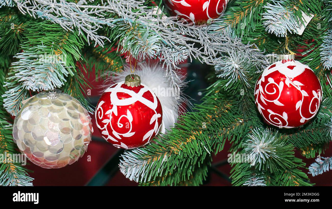 Eine Reihe festlicher Weihnachtsbaumschmuck, die an einem grünen Ast hängen Stockfoto