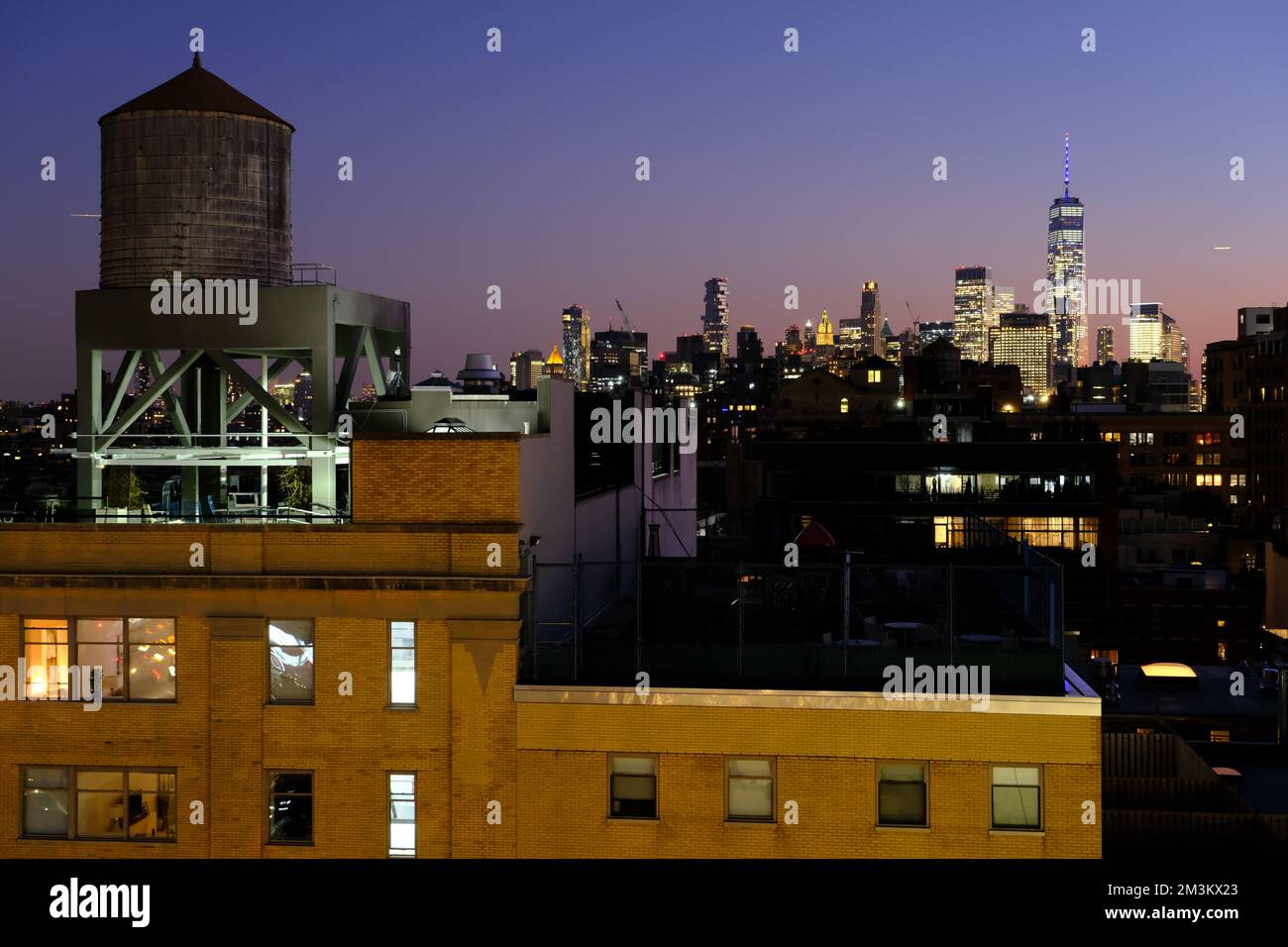 Blick in die Abenddämmerung auf die Skyline von Lower Manhattan und das One World Trade Center vom Meatpacking District mit einem Wasserturm auf dem Apartmentgebäude im Vordergrund. Manhattan. New York City. USA Stockfoto