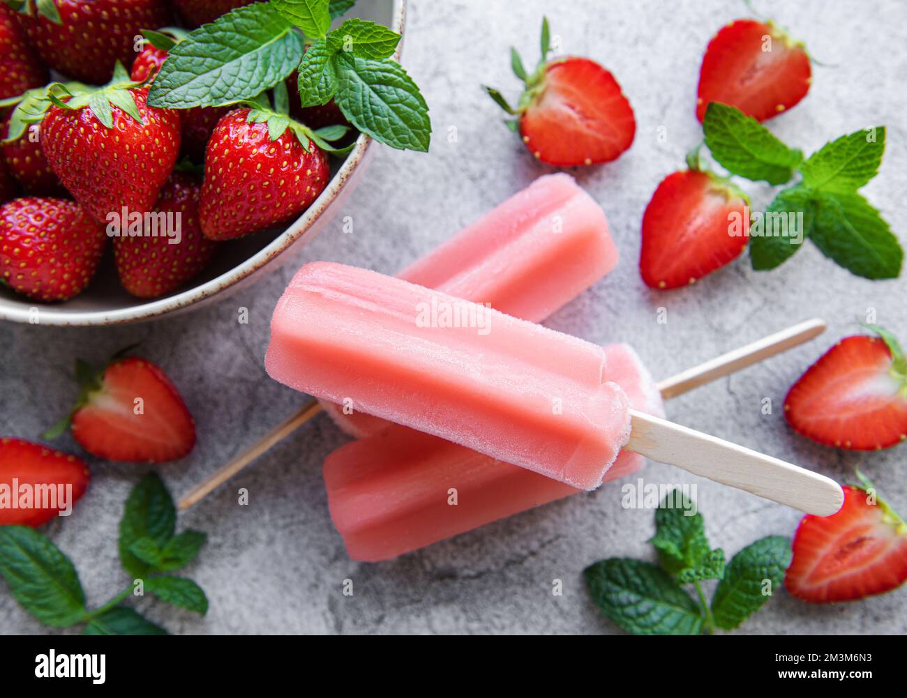 Hausgemachte gefrorene Erdbeer-Eis-Eiszapfen und frische Erdbeeren auf einem betonierten Hintergrund. Sommerdessert Stockfoto