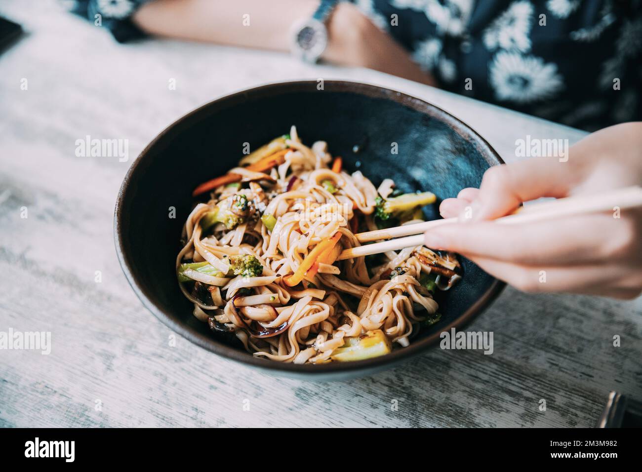 Frau, die asiatische Nudeln isst, udon mit Schweinefleisch im Café. Asiatische Nudeln udon mit Schweinefleisch Nahaufnahme in einer Schüssel auf dem Tisch Stockfoto