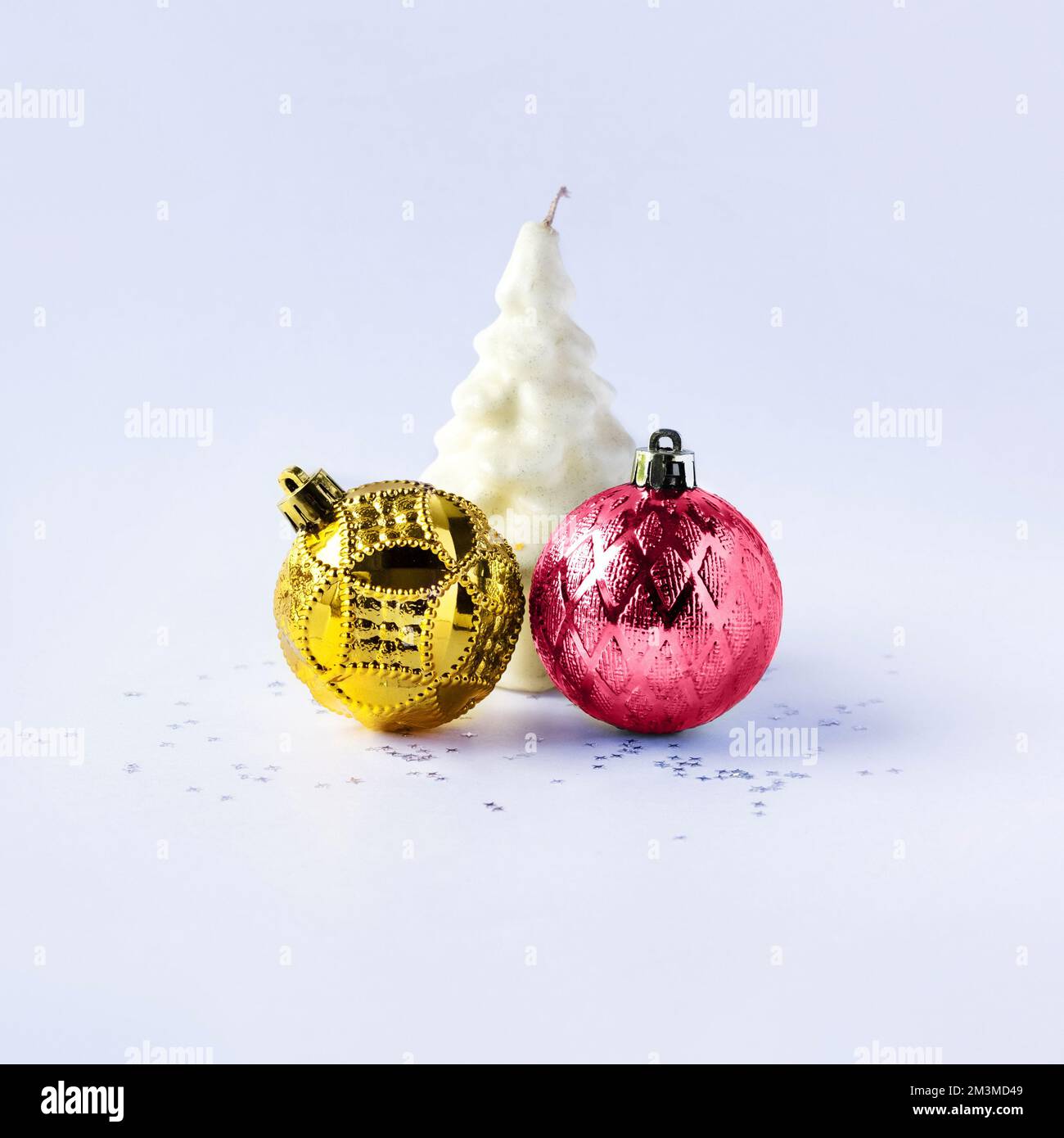 Weihnachtskomposition aus goldenen und magentafarbenen Weihnachtsbällen und einer weißen Weihnachtsbaumkerze auf grauem Hintergrund mit Sternen. Farbe Viva Magenta des Stockfoto