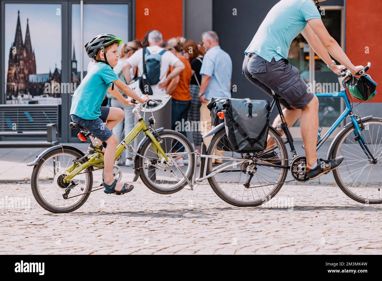 29. Juli 2022, Köln, Deutschland: Eine Sportfamilie - ein Vater mit einem Kind fährt Fahrrad durch die Straßen einer alten europäischen Stadt Stockfoto