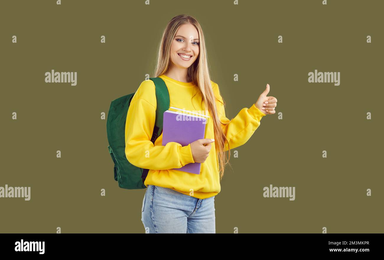 Glücklicher, erfolgreicher Student, der ein Notizbuch in der Hand hält, Daumen nach oben zeigt und lächelt Stockfoto