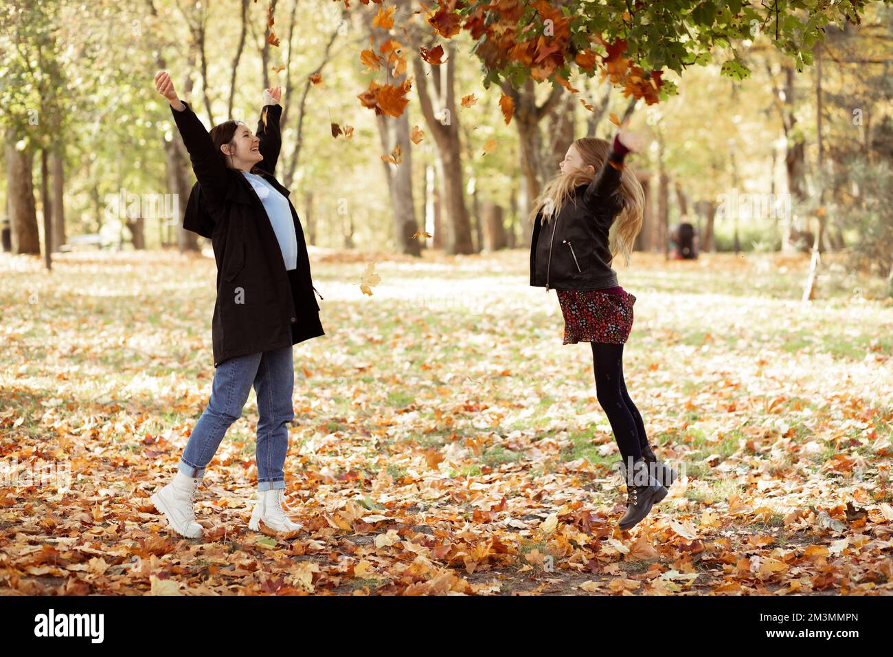 Ein Nebenblick auf eine lustige Familie von jungen Frauen, Mutter und Tochter im Teenageralter, die im Herbst Blätter in den Wald werfen. Stockfoto