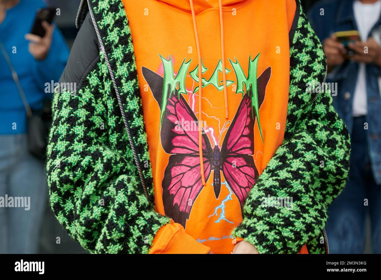 MAILAND, ITALIEN - 24. SEPTEMBER 2022: Frau mit orangefarbenem MSGM-Hoodie mit Schmetterling und Hahnentrittmuster in Schwarz und Grün vor der MSGM-Modenschau, Mailand Stockfoto