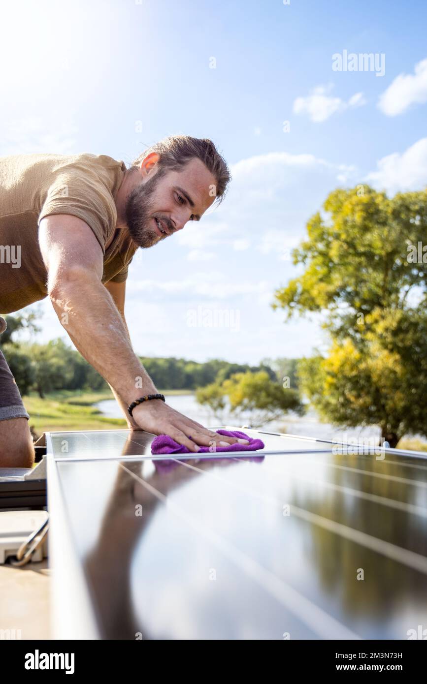 Mann reinigt die Sonnenkollektoren auf dem Dach eines Wohnwagens mit einem Tuch Stockfoto