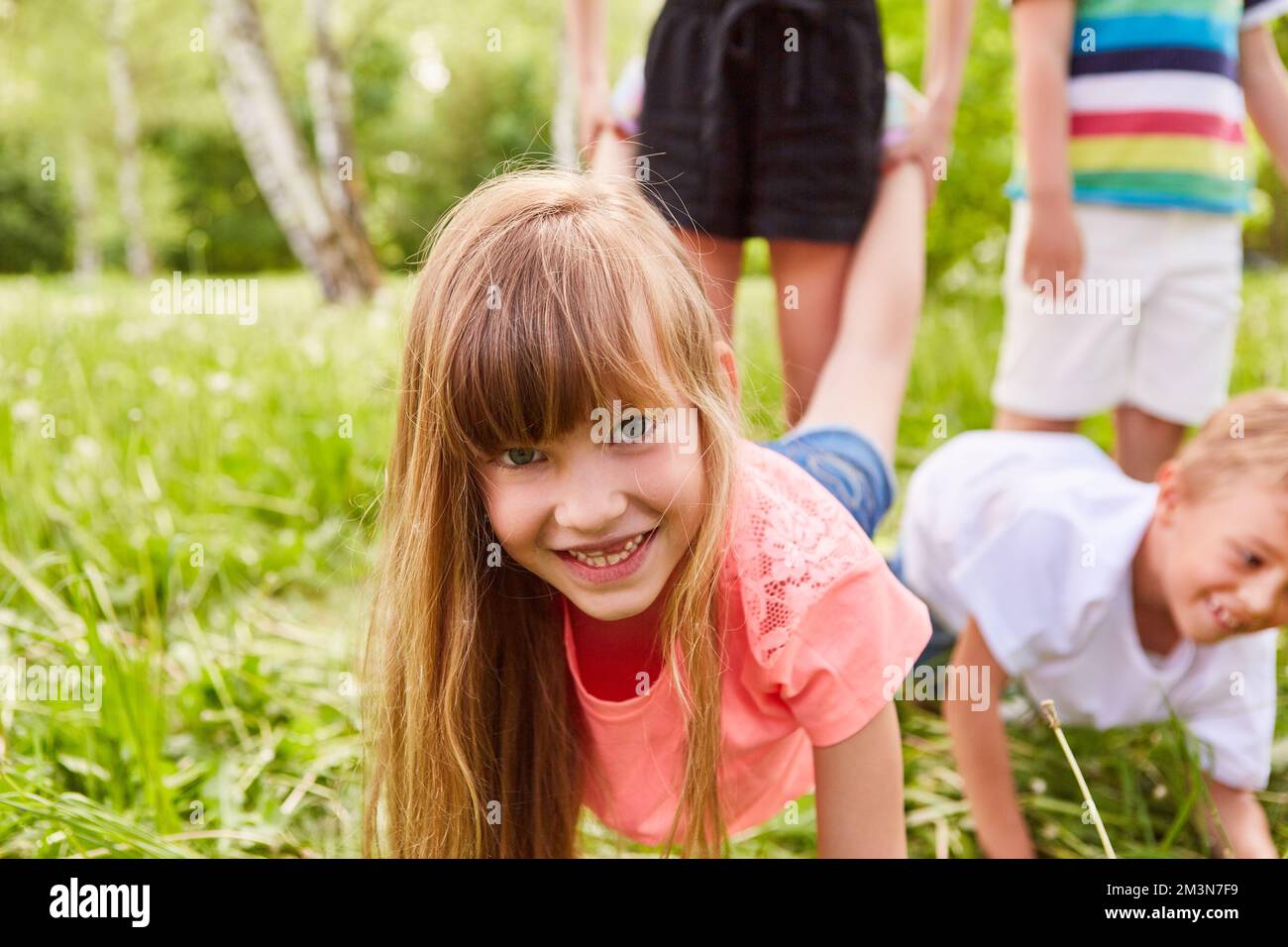 Porträt eines glücklichen Mädchens, das mit Freunden während eines Schubkarren-Rennens im Garten spielt Stockfoto