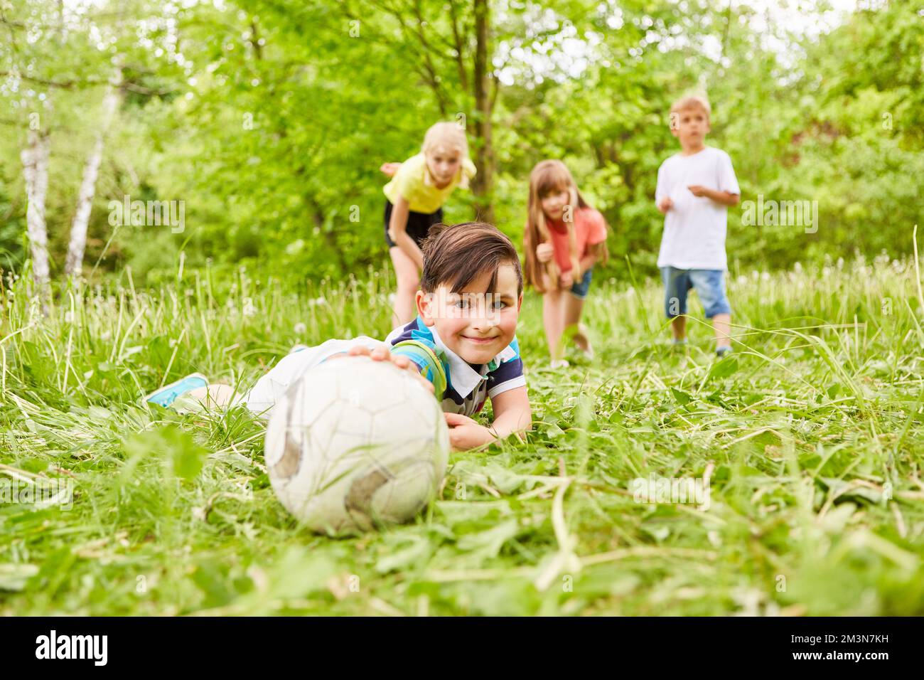 Porträt eines lächelnden Jungen, der Fußball mit Freunden im Garten berührt Stockfoto