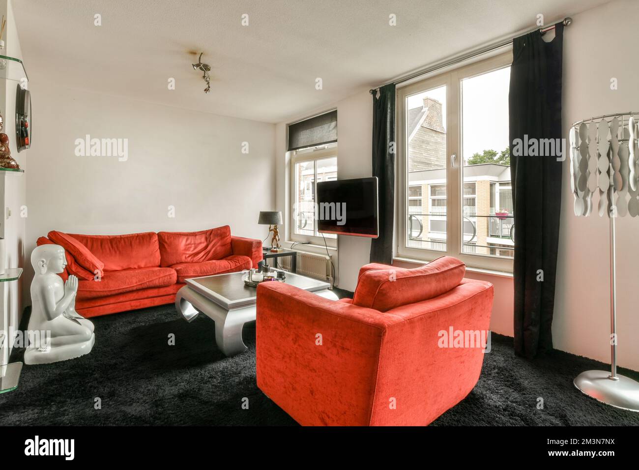 Wohnzimmer mit komfortablem rotem Sofa und Fernseher gegen Fenster im modernen Apartment Stockfoto