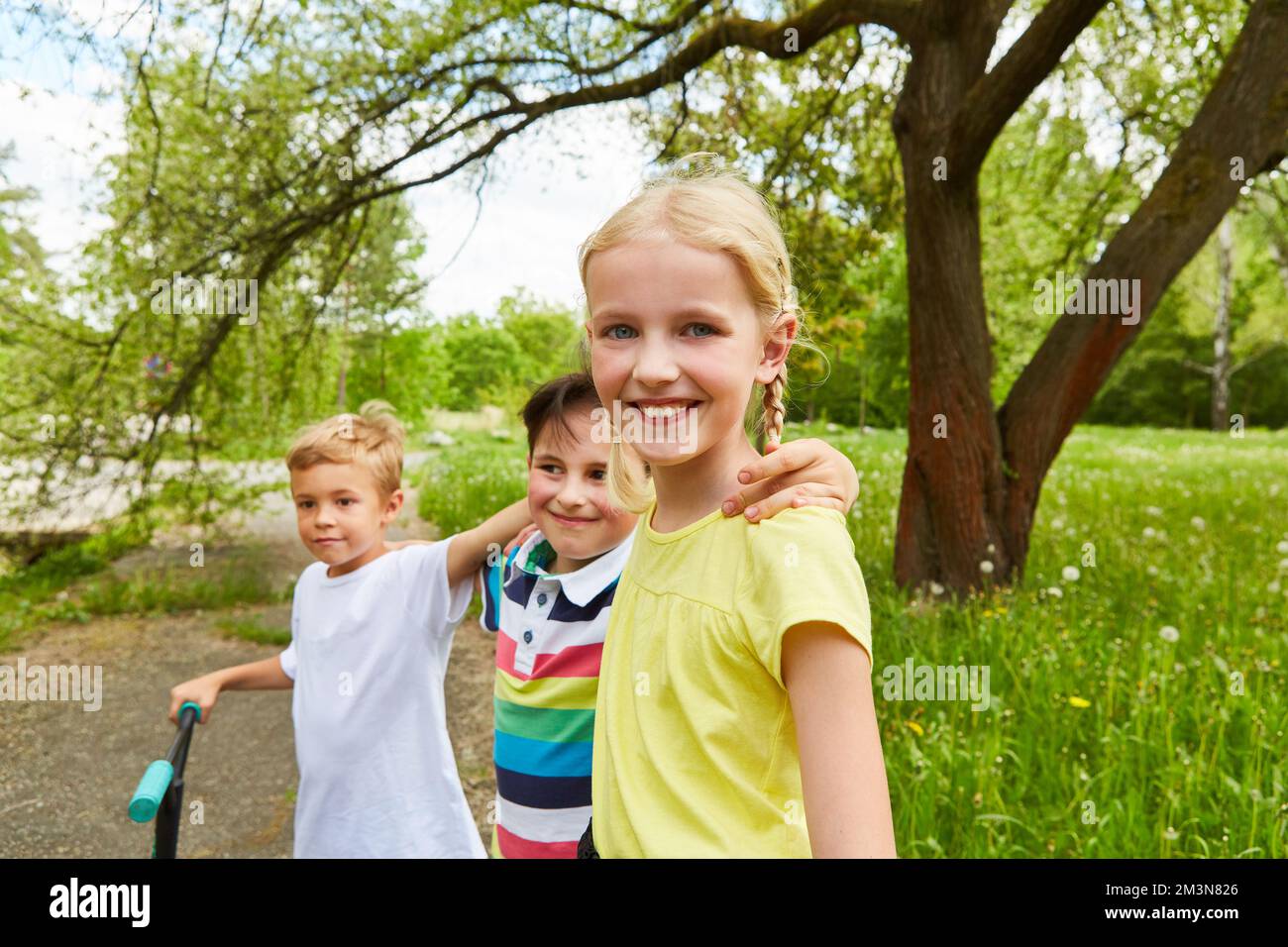 Glückliches Mädchen, das während der Sommerferien bei männlichen Freunden mit Händen an der Schulter im Garten steht Stockfoto