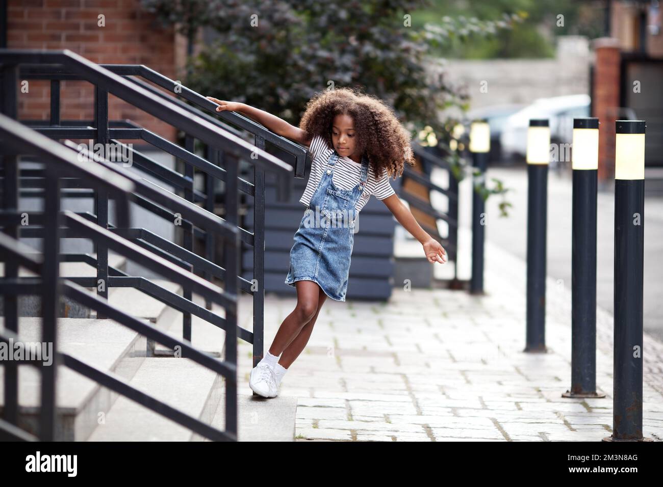 Ein afroamerikanisches Mädchen geht die Treppe auf der City Street runter. Das Porträt des Kindes im Jeansrock und T-Shirt im Freien Stockfoto