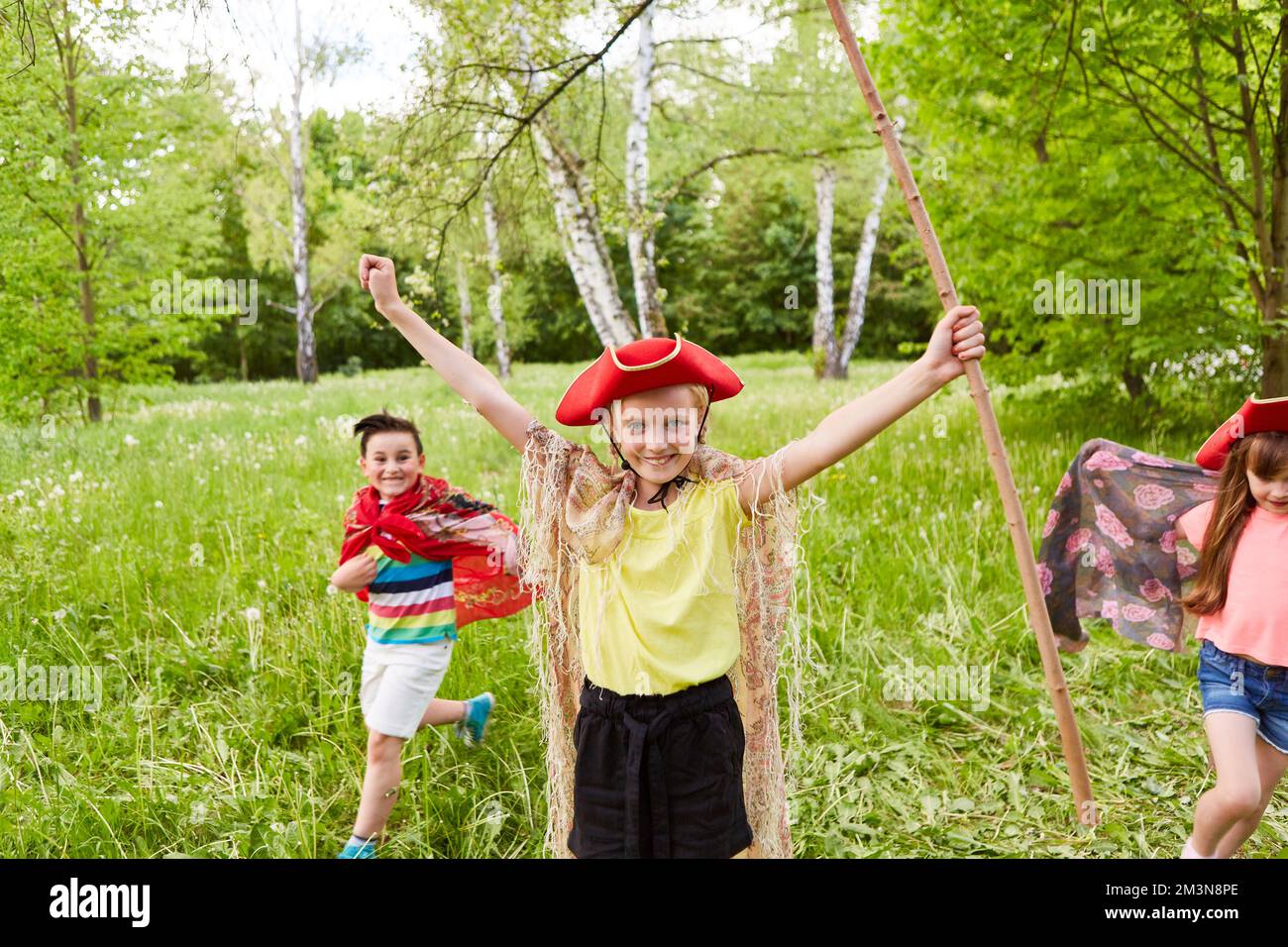 Porträt eines glücklichen Mädchens mit Tricornhut und Stäbchen, die von Freunden ausgestreckt im Gras stehen Stockfoto