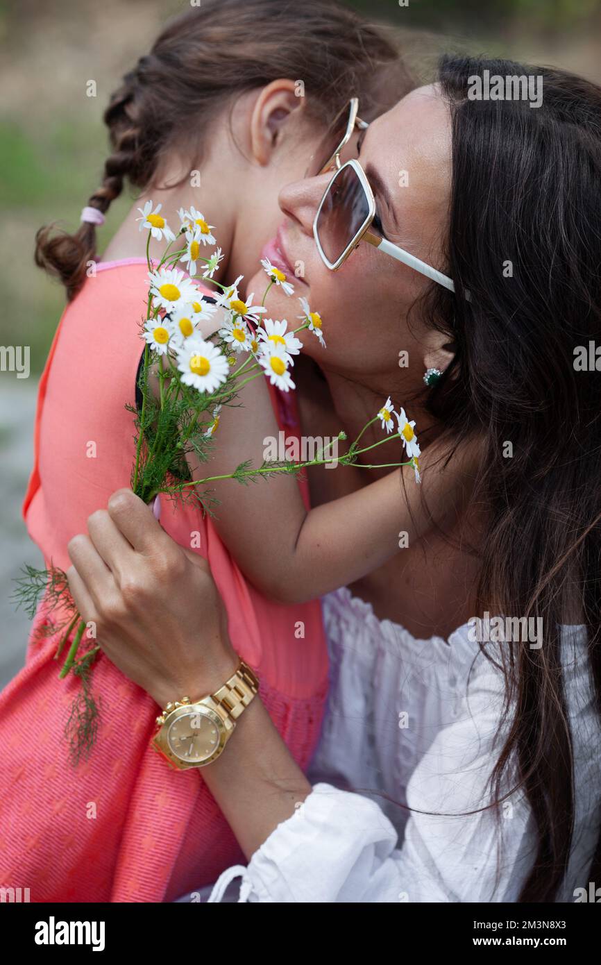 Nahaufnahme des Porträts von Mutter umarmt Tochter Kind und hält Kamillenblumen. Muttertag Stockfoto