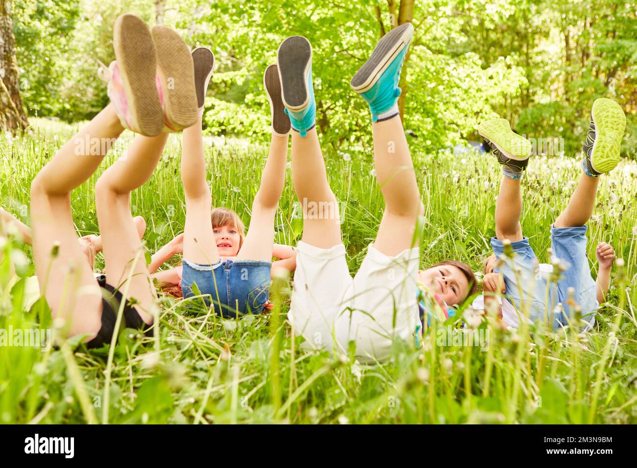 Verspielte, multirassische, männliche und weibliche Freunde mit den Beinen oben auf der Wiese während der Sommerferien Stockfoto