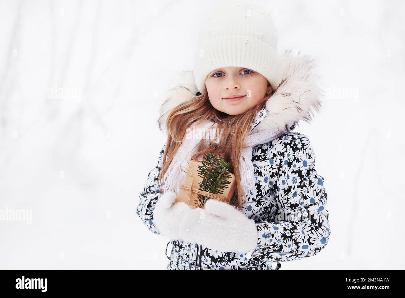 Hübsches kleines Mädchen mit weihnachtsgeschenk in warmer Kleidung im Winter auf weißem Schneehintergrund. Outdoor Winterporträt schönes kleines Kindermodell mit Stockfoto