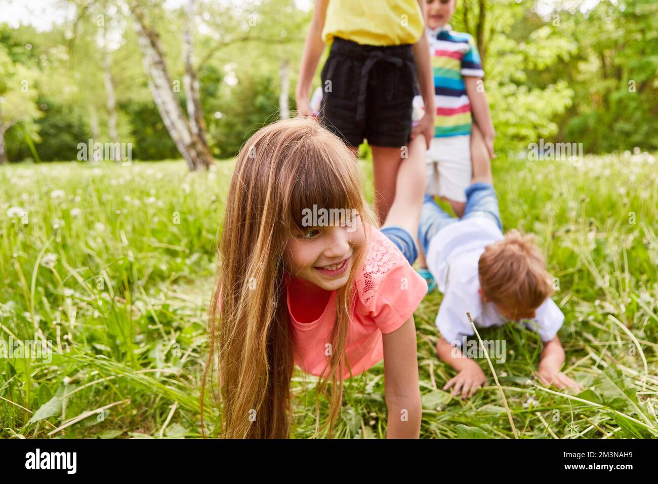 Verspieltes Mädchen mit männlichen Freunden, das während des Urlaubs im Park einen Rollkarren-Wettkampf spielt Stockfoto