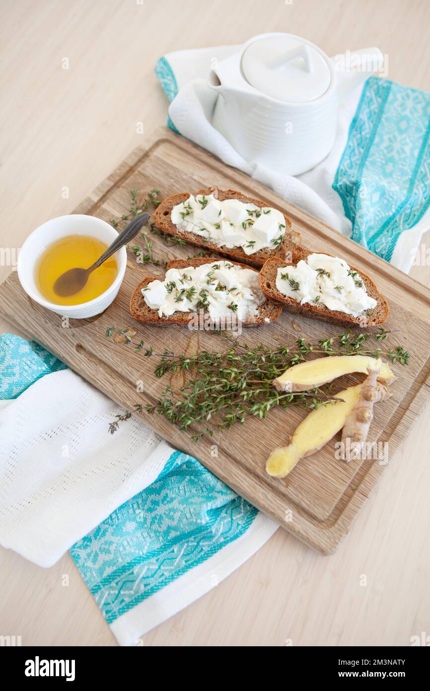 Still Life Sandwiches mit Käse, Thymian, Ingwer und Tee mit Honig. Tischdecken zum Frühstück auf Holzbrett und Stoffservietten. Tischablage Stockfoto