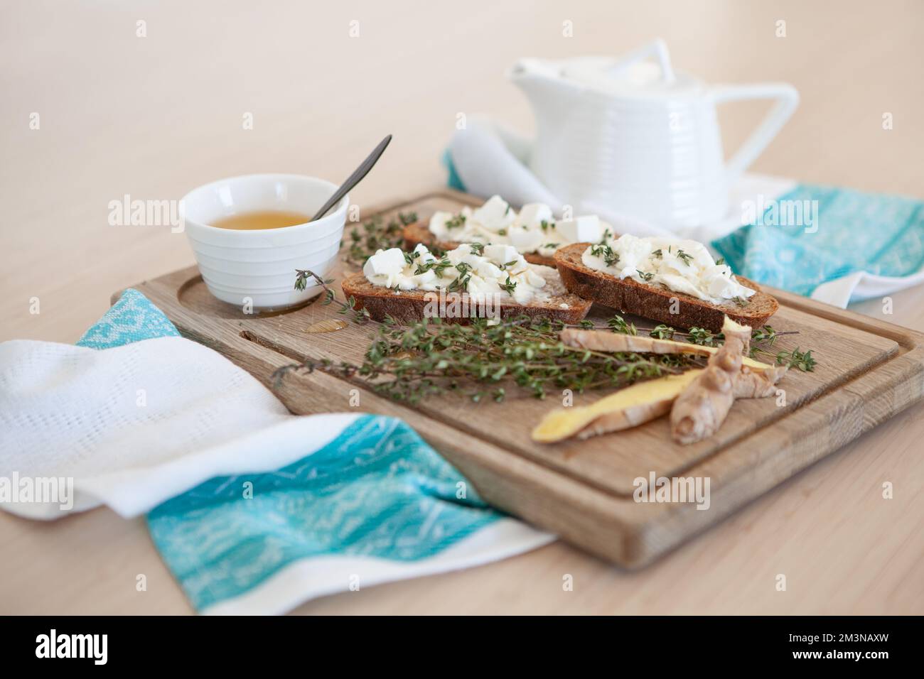 Sandwiches mit Butter, Thymian, Ingwer und Tee mit Honig. Tischaufstellung auf Holzbrett und Stoffserviette. Tischfliehen und Stillleben Stockfoto