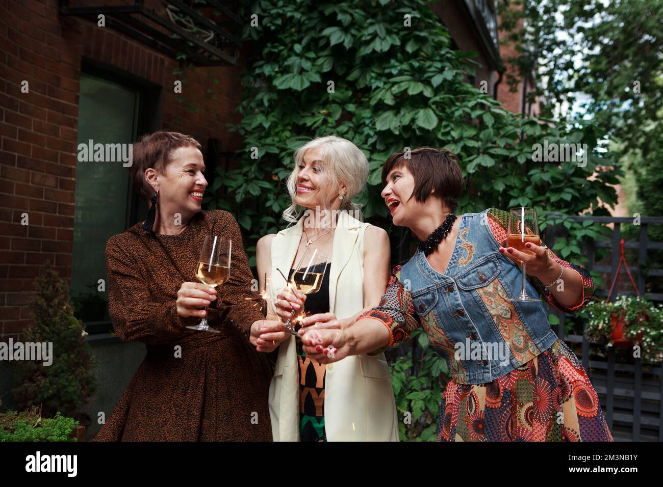 Freunde von Frauen mittleren Alters feiern, haben Spaß mit Sekt und Gläsern alkoholischen Weins oder Champagner auf einer Party im Freien Stockfoto