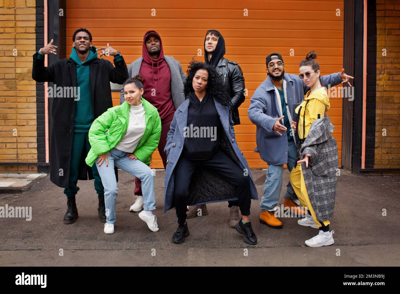 Eine multiethnische Gruppe junger Hipster tanzt vor orangefarbenem Hintergrund auf der Straße der Stadt zusammen. Vielfältige, stilvolle Menschen im Freien, Jugendkultur Stockfoto