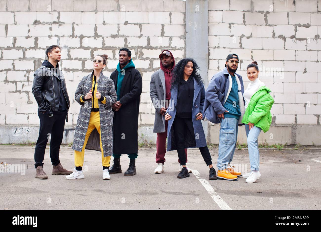 Eine multiethnische Gruppe junger Hipster steht gemeinsam auf der Straße vor grauen Ziegelmauern. Verschiedene stilvolle Menschen in Oberbekleidung, Outdoor, Jugendkultur Stockfoto
