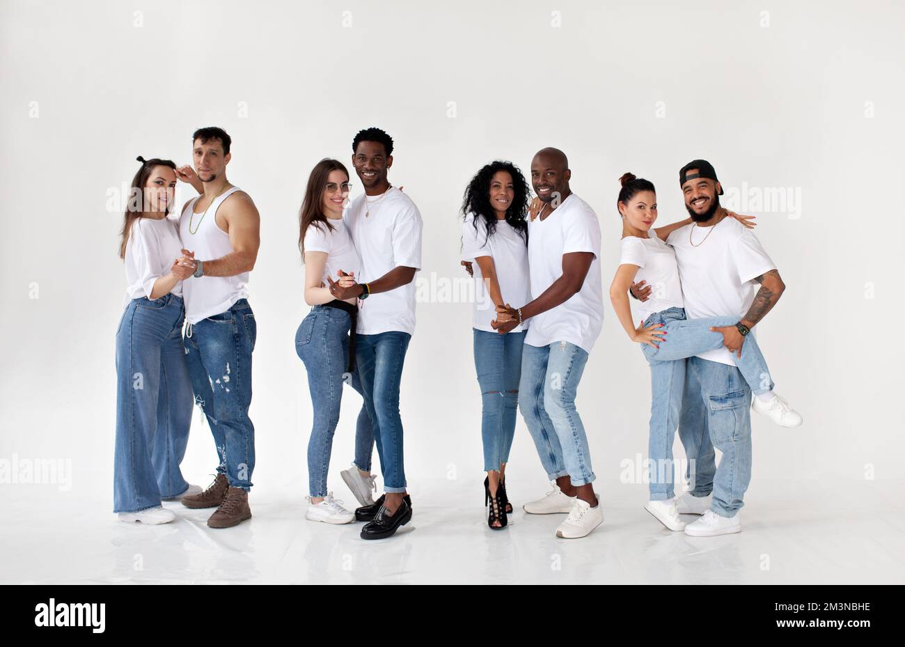 Eine Gruppe junger, glücklicher, multiethnischer Paare, isoliert auf weißem Hintergrund, die in die Kamera schauen und lächeln, weiße T-Shirts und Jeans tragen Stockfoto