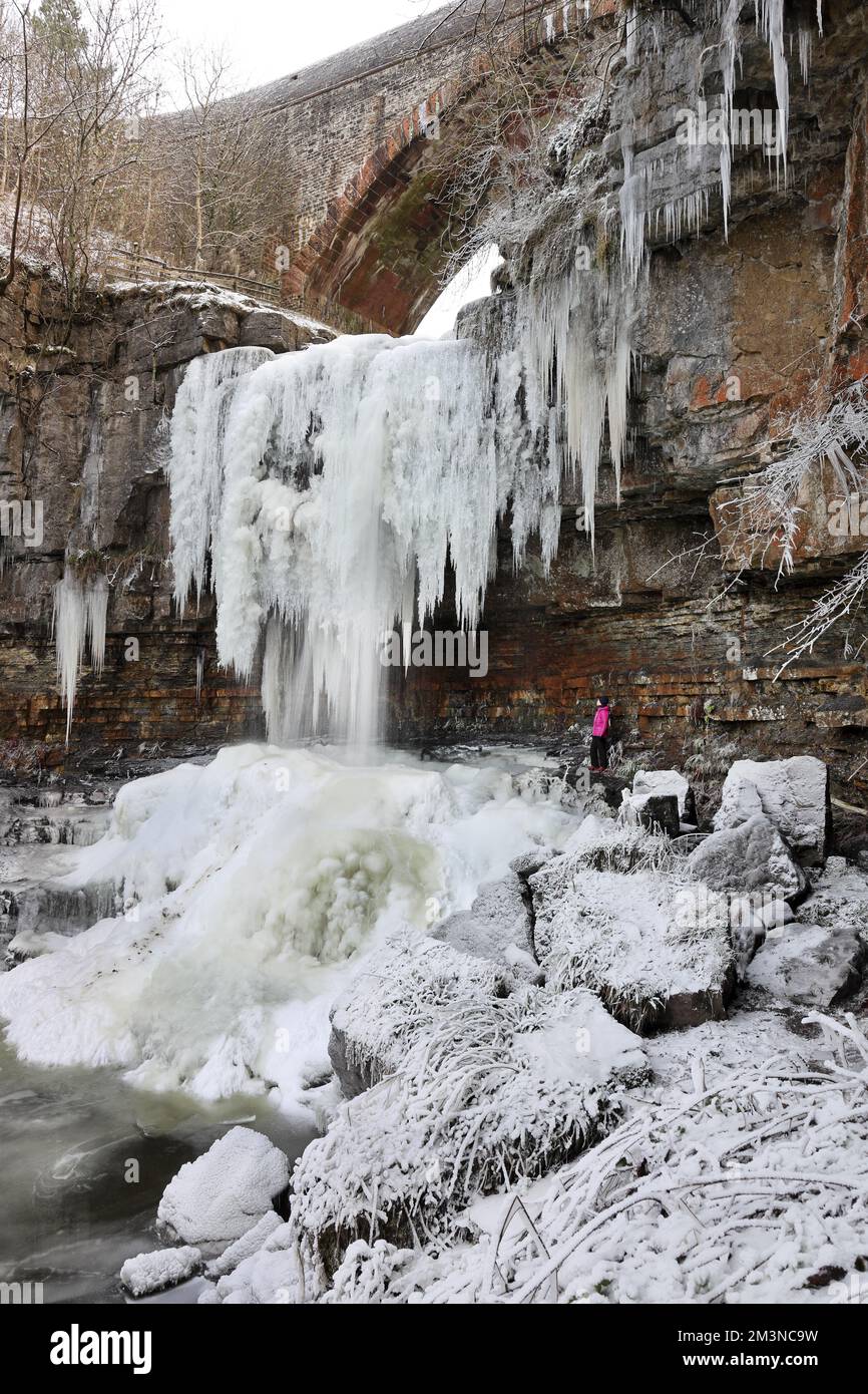 Ashgill Force, Garrigill, Cumbria, Großbritannien. 16.. Dezember 2022 Wetter in Großbritannien. Ein Wanderer genießt das Spektakel der riesigen Eiszapfen, die nach einer weiteren Nacht unter den Temperaturen in Cumbria vom gefrorenen Wasserfall der Ashgill Force in der Nähe von Garrigill hängen. Kredit: David Forster/Alamy Live News Stockfoto