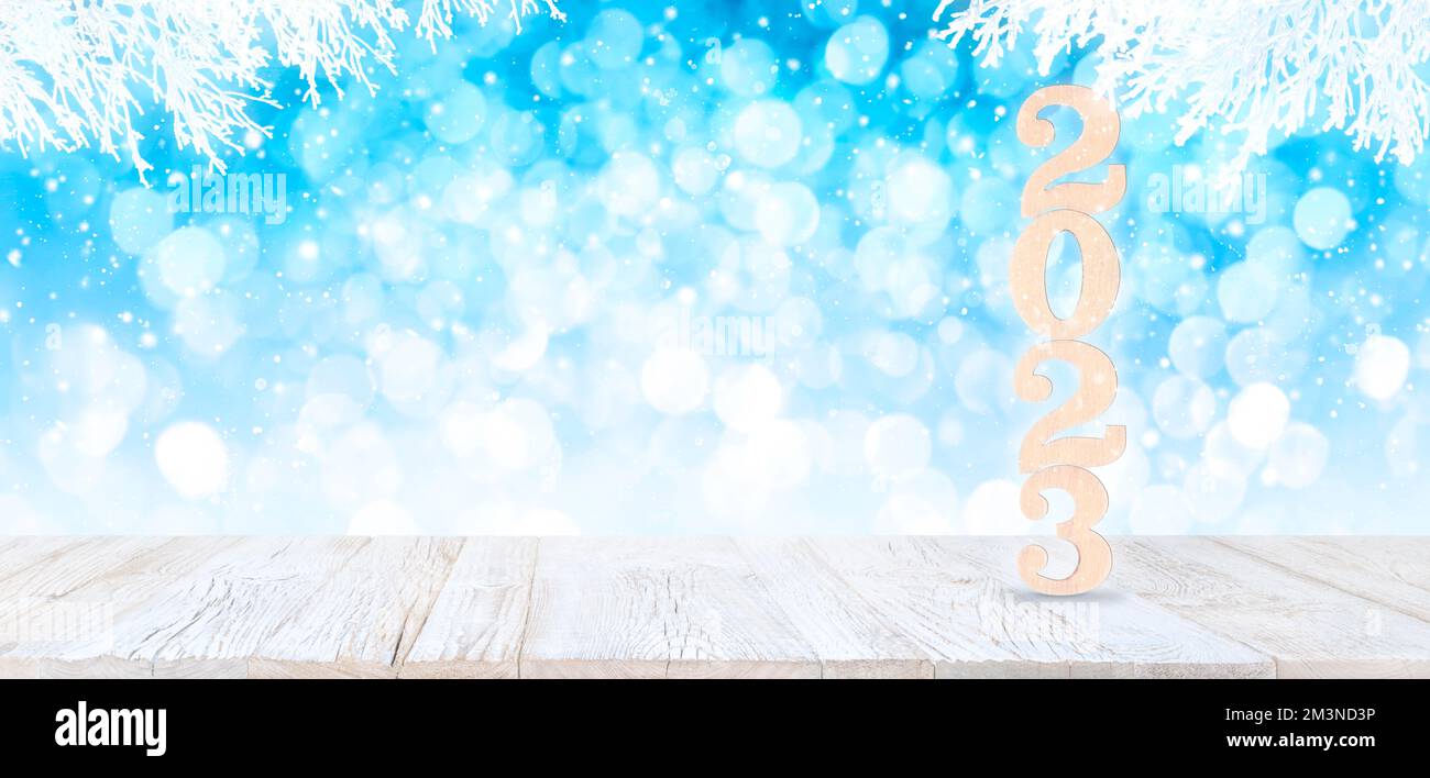 Frohes neues Jahr 2023 Holzzahlen auf weißem altem Plankentisch mit Blick auf den hellblauen Bokeh-Winterhintergrund mit weißen schneebedeckten Zweigen Stockfoto