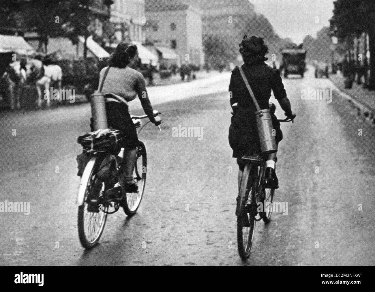 Zwei französische Frauen radeln in Paris zur Arbeit, mit Gasmasken, die in Kanistern über ihre Schultern geschleudert wurden. Datum: 1939 Stockfoto
