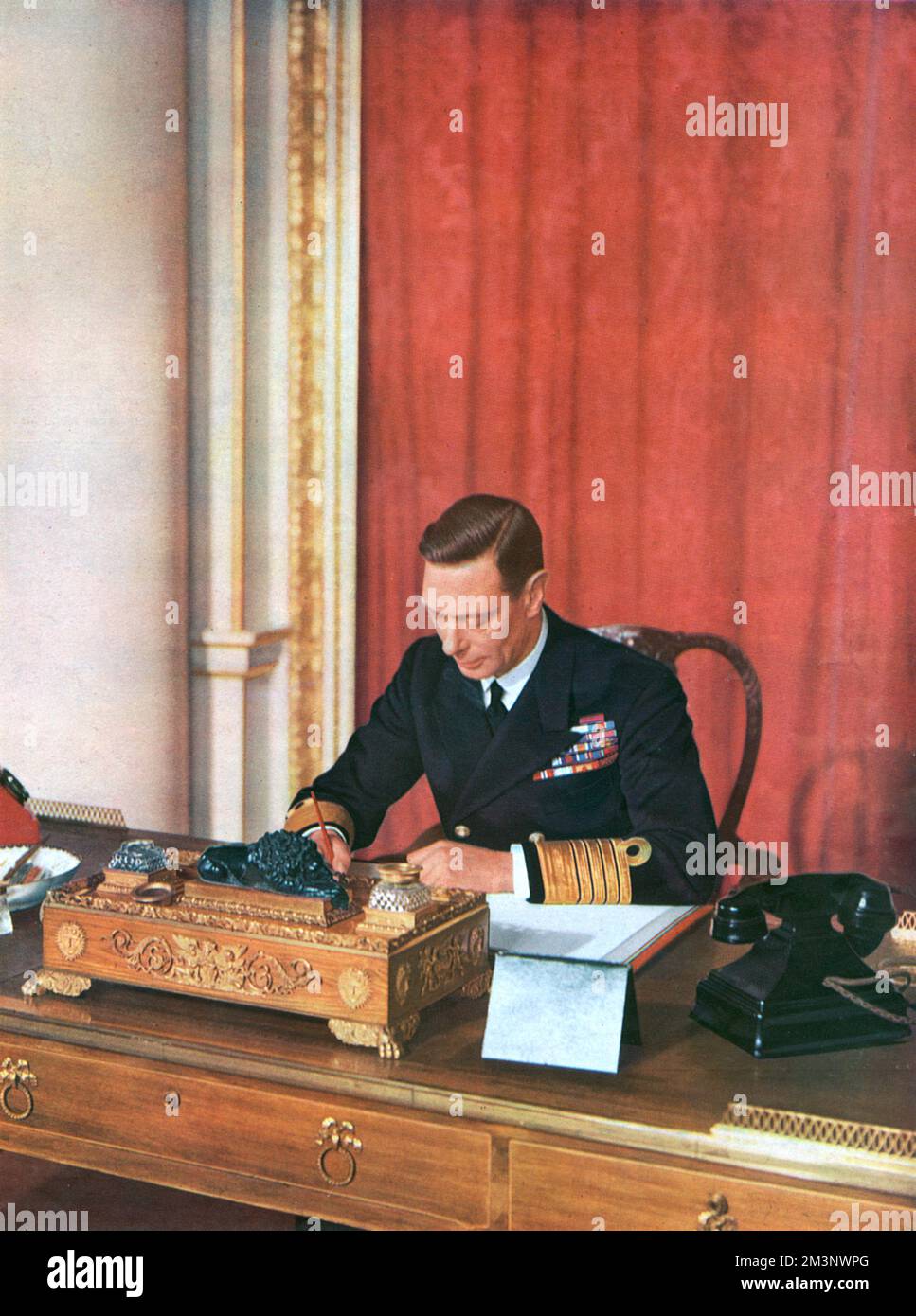 König George VI. (1895 - 1952), im Mai 1942 in Marineuniform an seinem Schreibtisch im Buckingham Palace. Eine exklusive Fotosession, die speziell für die illustrierten London News zum hundertsten Geburtstag dieser Zeit gewährt wurde. Datum: 1942 Stockfoto