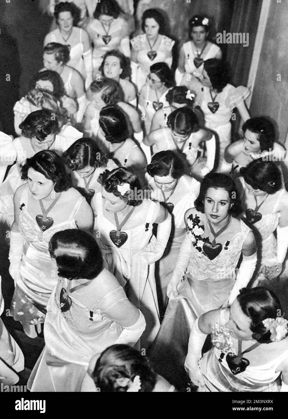 Alles in Weiß mit scharlachroten Satinherzen um den Hals (ein Geschenk von Schiaparelli), Debütantinnen auf dem Queen Charlotte's Ball von 1939. Datum: 1939 Stockfoto