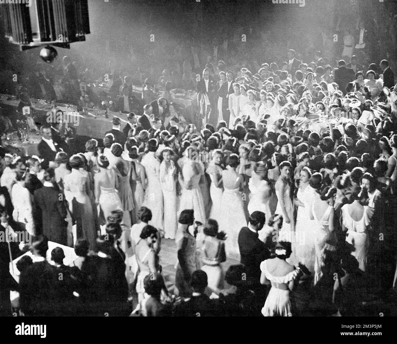 Queen Charlotte's Ball im Grosvenor House zeigt Debütantinnen in ihrem weißen Kleid um den Kuchen, nachdem er von der Herzogin von Kent geschnitten wurde, bereit, Stücke zu den 1500 Gästen zu bringen. Datum: 1937 Stockfoto