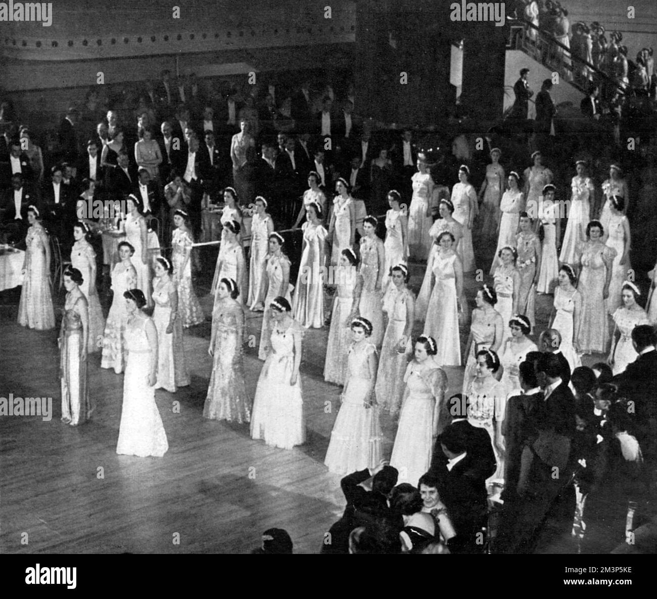 Glänzend in gezackten Reihen: Debütantinnen, die während Queen Charlotte's Ball auf dem Boden des Ballsaals vor dem traditionellen Schneiden des Kuchens, durchgeführt in diesem Jahr der Krönung von der Herzogin von Kent. Datum: 1937 Stockfoto