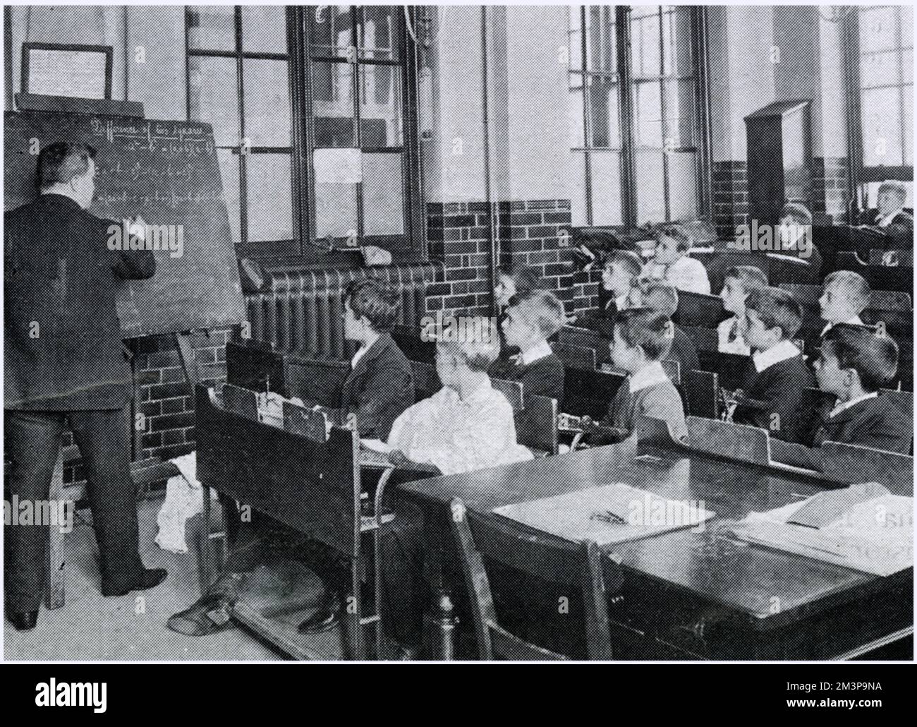 Konventionelle Art des Unterrichts, bei der alle Schüler nach vorne schauen, während der Lehrer auf das Schwarze Brett schreibt. Datum: 1906 Stockfoto