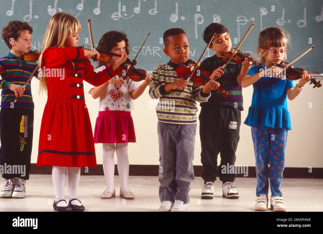 Gruppe von 6 kleinen Kindern, die vor dem Klassenzimmer Geigen spielen Stockfoto