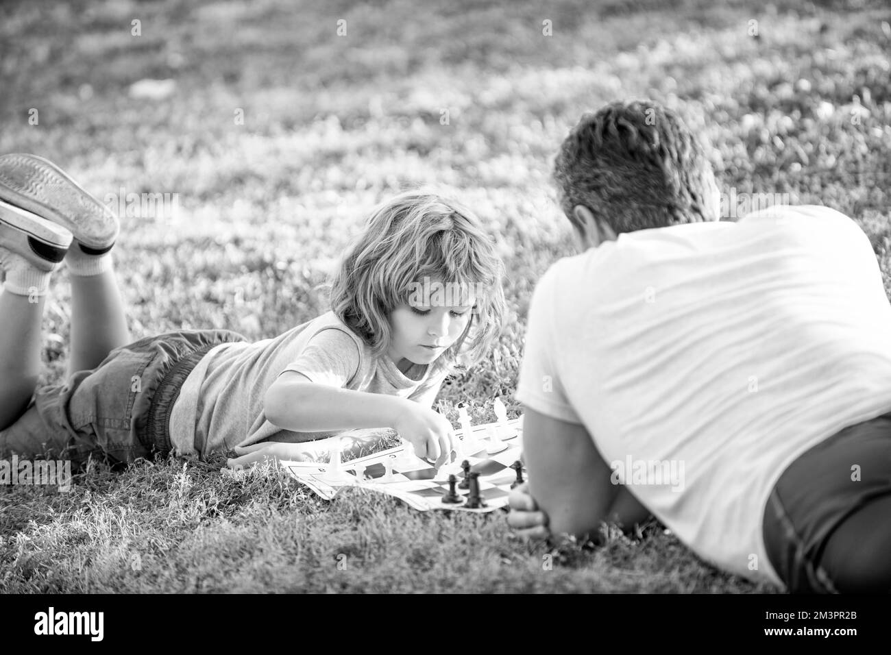 Glückliche Familie von Vater und Sohn Kind spielen Schach auf grünem Gras im Park im Freien, Tutorenschaft Stockfoto