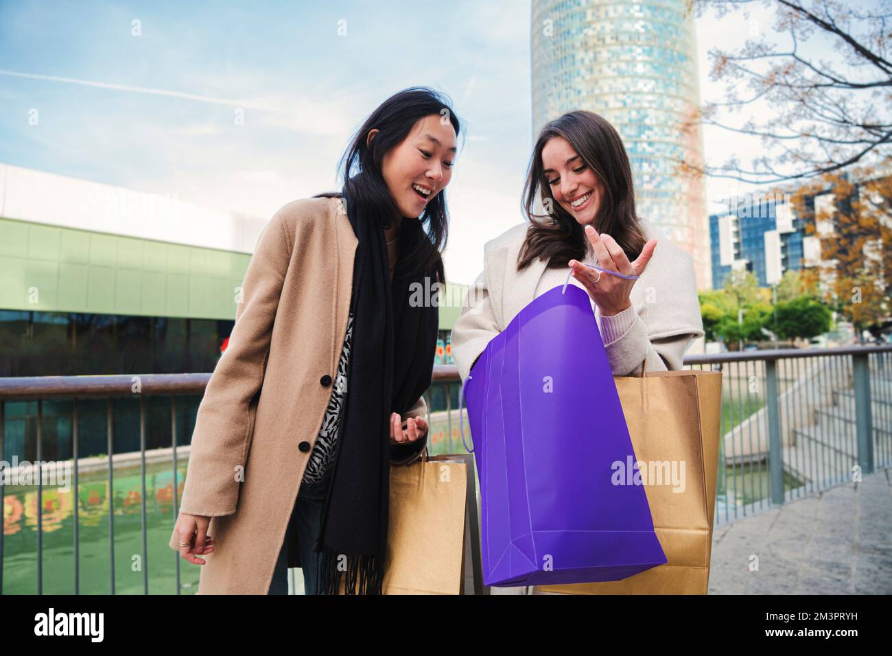 Zwei junge, glückliche Frauen überraschten, als sie in die Einkaufstasche schauten, die Kleidung, die sie gerade in der Verkaufswoche gekauft hatten. Ein paar Weibchen wurden von dem Rabatt in einem Laden außerhalb des Einkaufszentrums vertrieben. Hochwertiges Foto Stockfoto
