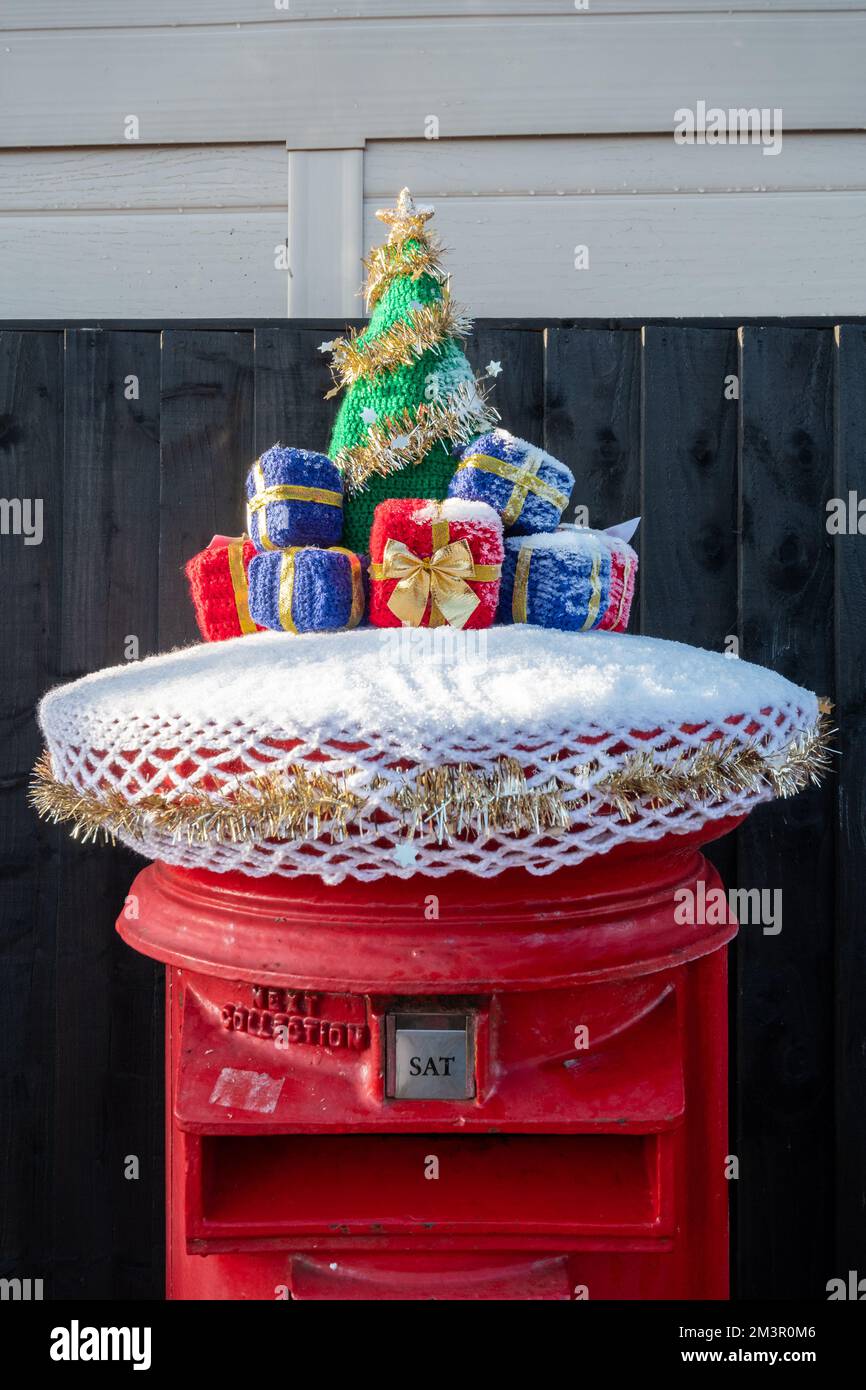 Weihnachtspostkastenaufsatz, Häkelchen oder gestrickter weihnachtsbaum und Geschenke auf rotem königlichem Briefkasten, England, Großbritannien, im Dezember 2022 Stockfoto