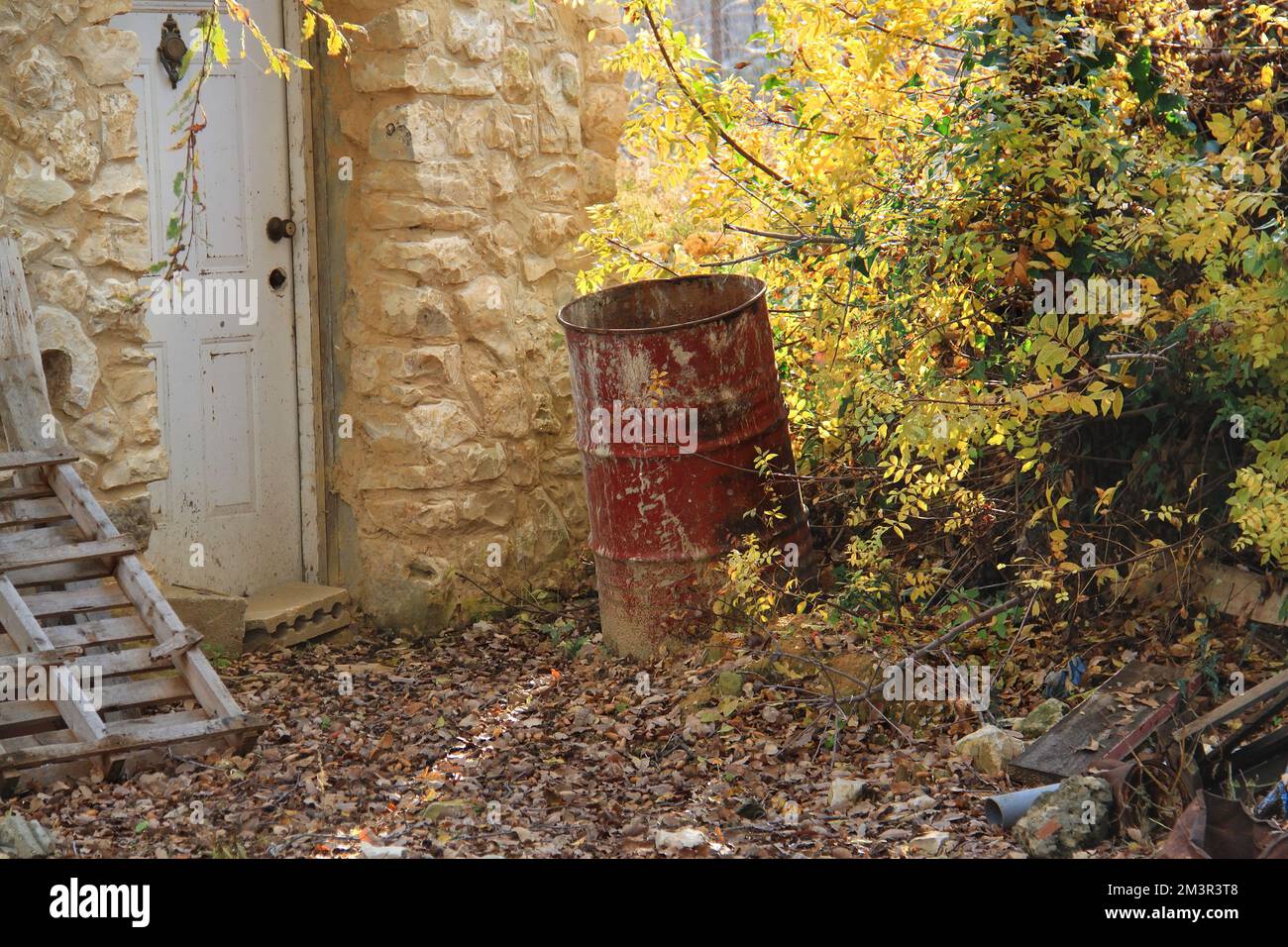 Ein rostiges rotes Fass in einem Hof mit Eicheln auf dem Boden. Stockfoto
