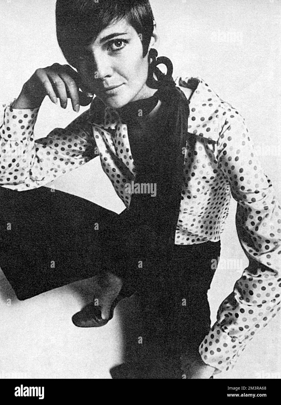 Model trägt ein fliederfarbenes gepunktetes Tricel-Shirt mit tiefer Pflaumenhose. Beide von Londonus. Die flachen Lederschuhe sind von Russell und Bromley und die Korb-Ohrringe von Corocraft. Das Outfit wurde zusammengestellt, um die Persönlichkeit der Art Mädchen zu reflektieren, die Mouchi-Parfüm tragen könnte, das zu dieser Zeit beliebt war. Datum: 1966 Stockfoto