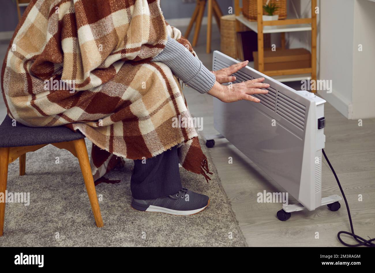 Ein Mann sitzt im Winter zu Hause, fühlt sich kalt und wärmt seine Hände mit einer elektrischen Heizung Stockfoto
