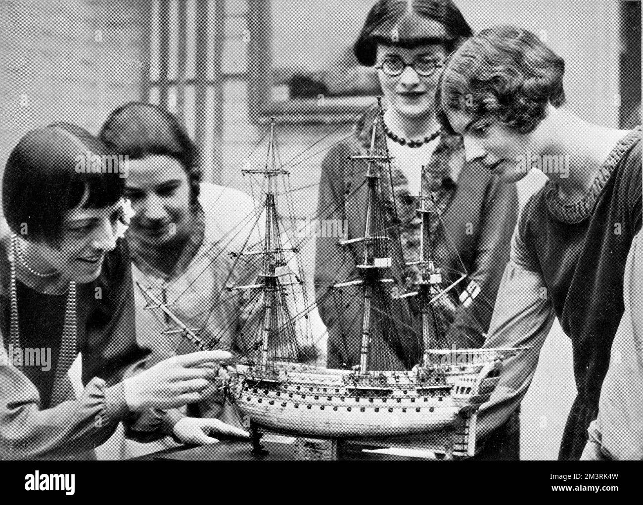 Vier Frauen, die über ein Modellschiff schauen, auf einer Ausstellung mit alten Schiffen und Karten. Damals waren diese Themen in der Inneneinrichtung sehr beliebt. 1927 Stockfoto