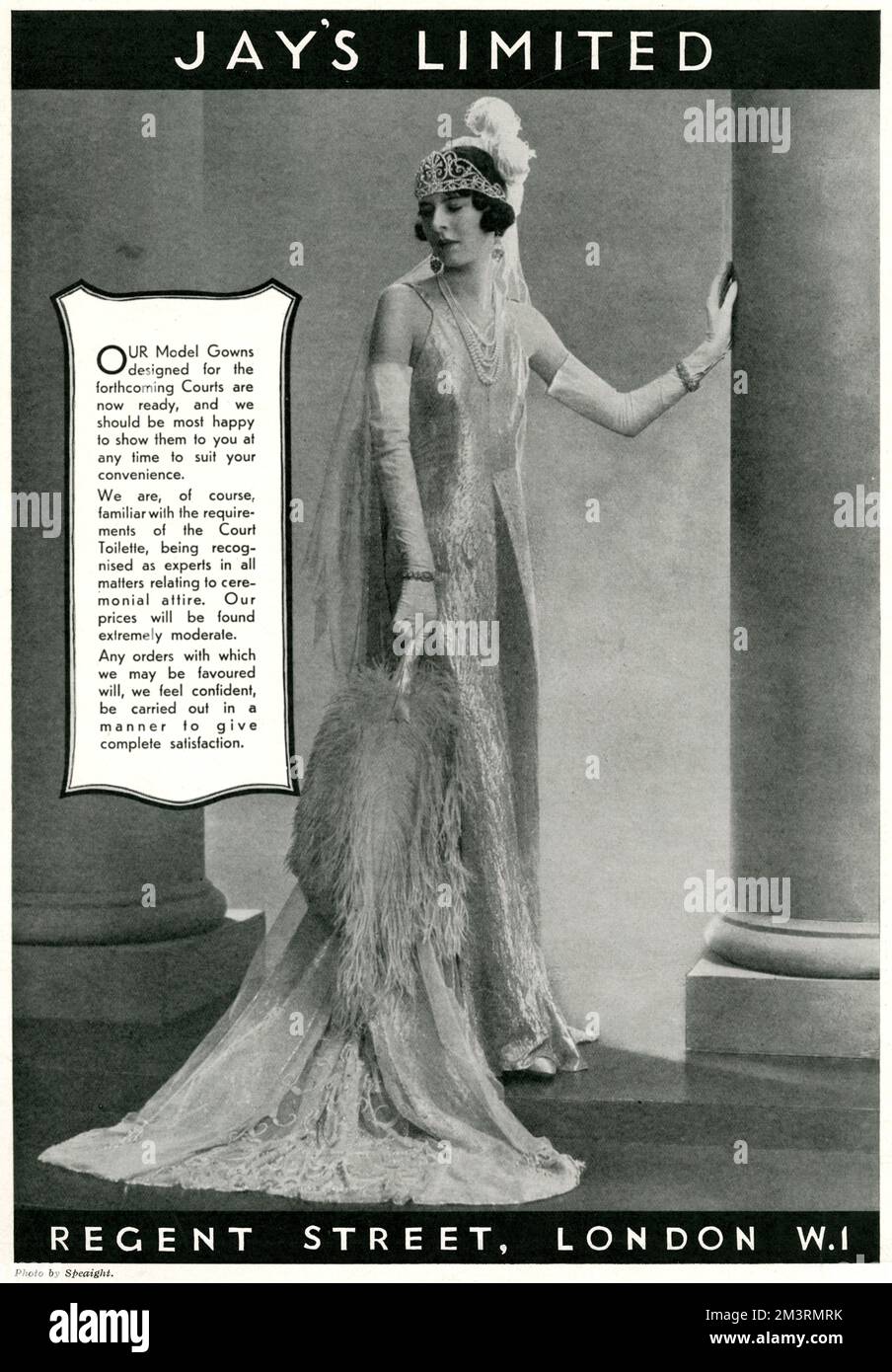 Begrenzte Anzahl an Gerichtskleidern, verfügbar bei „Jay's“. Ein Model mit einem wunderschönen, schlanken Kleid, weißen langen Handschuhen, Zug, Federn und Diadem. 1933 Stockfoto