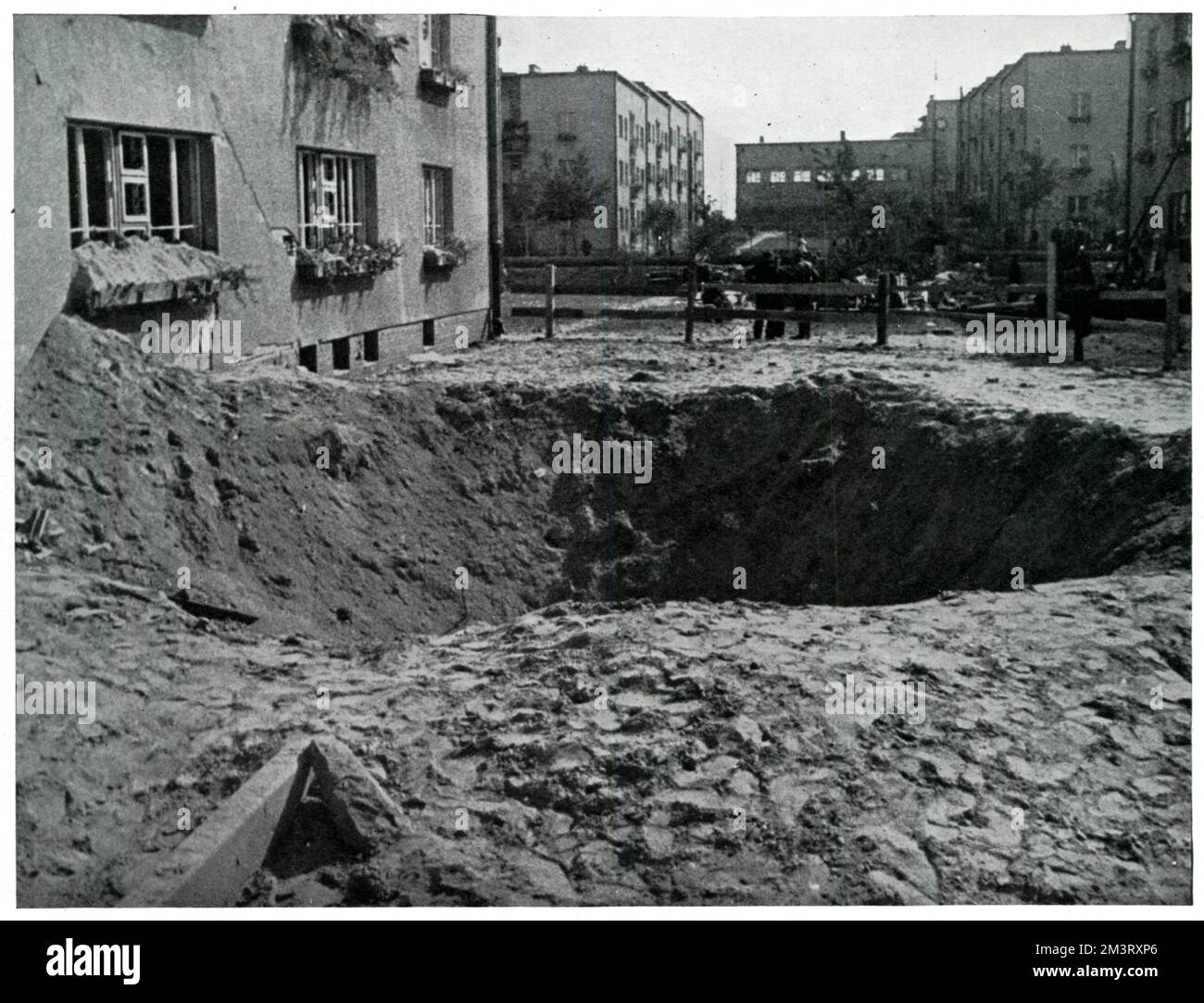 Großer Bombenkrater in einer Warschauer Straße neben einem Haus, das strukturell intakt zu sein scheint, obwohl die Fenster bei der Explosion verloren gingen, die durch die deutsche Belagerung und Luftangriffe auf die Hauptstadt im September 1939 ausgelöst wurde. September 1939 Stockfoto