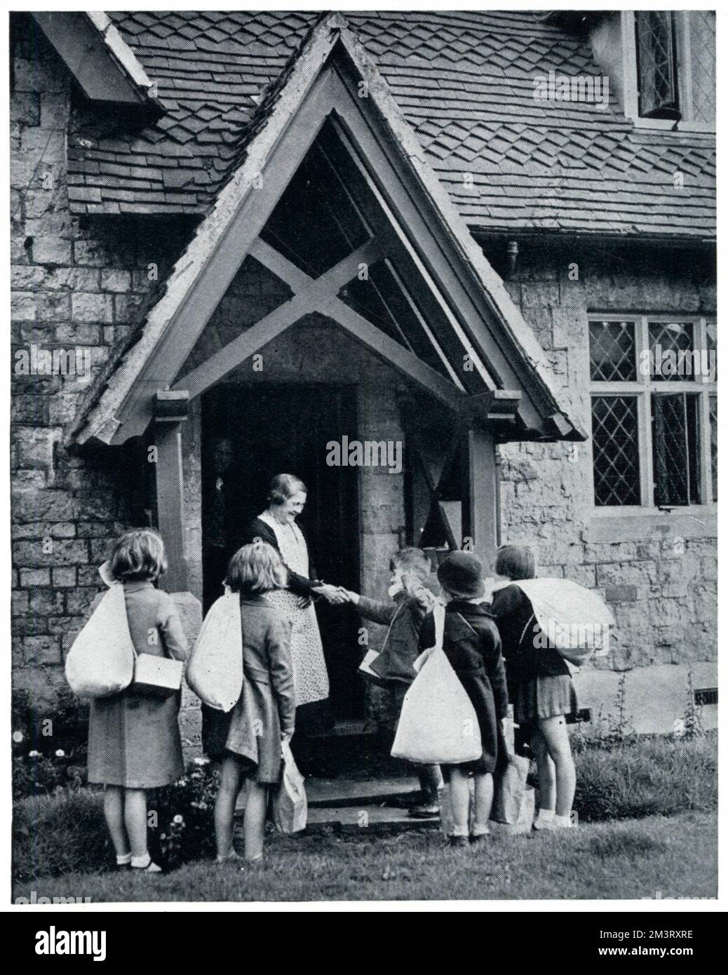 Eine Gruppe evakuierter Kinder wird von einer lächelnden Frau und einem Mann begrüßt und erhält ihre Taschen bei der Ankunft auf dem Land. September 1939 Stockfoto