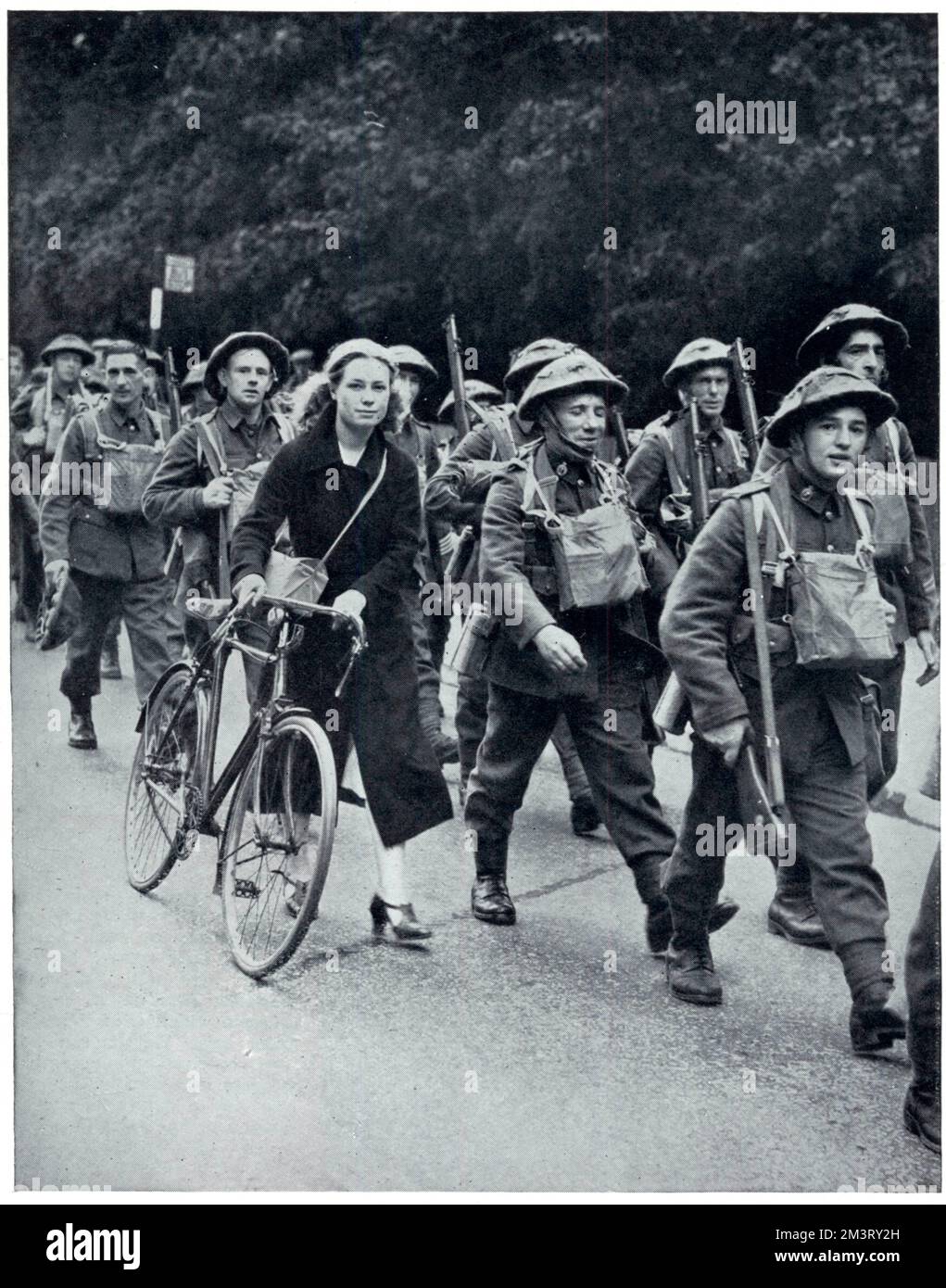 Britische Soldaten marschieren in voller Uniform bis zu ihrem Einschiffungsort für die Westfront, einige Wochen nach Kriegsausbruch. Sie werden von einer Frau begleitet, vielleicht um sie zu verabschieden, aber die Sphärenkommentare auf ihren Helmen, die ein neues Merkmal der britischen Militäruniform waren. Datum: 1939 Stockfoto