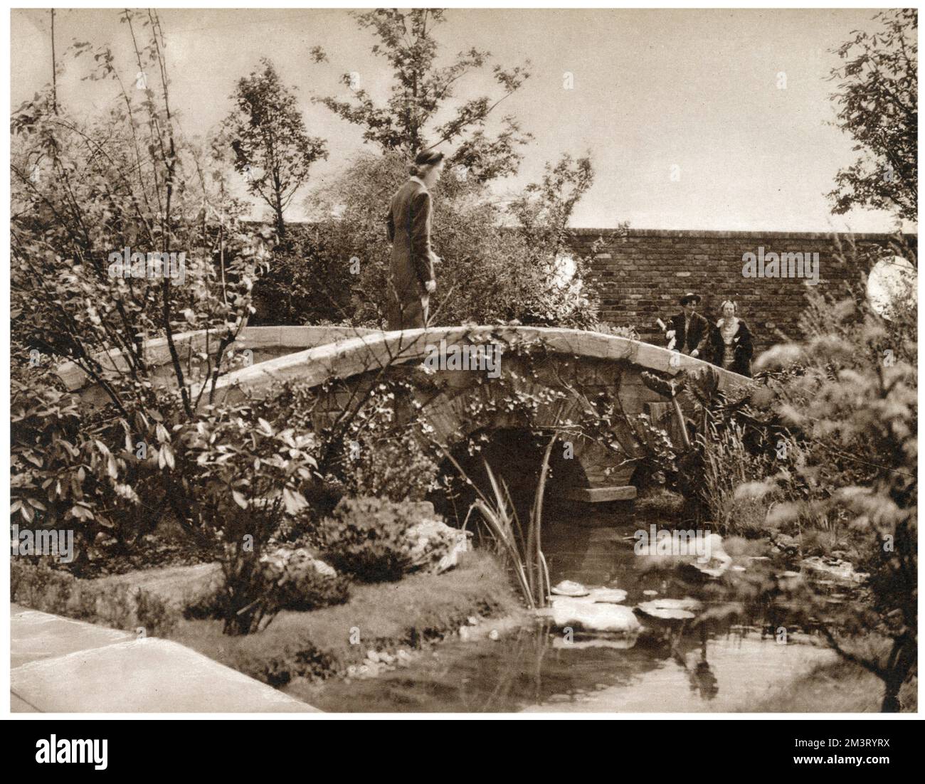 Eine Steinbrücke, die sich über den Fluss erstreckt, umgeben von Bäumen im Old English Garden, Teil des Dachgartens auf der Spitze von Derry und Toms in der Kensington High Street, Eröffnet im Jahr 1938 und zugänglich für die Öffentlichkeit, die einen Schilling für die Einreise bezahlt hat, um Geld für das Queens Institute of District Nursing zu sammeln. Datum: 1938 Stockfoto