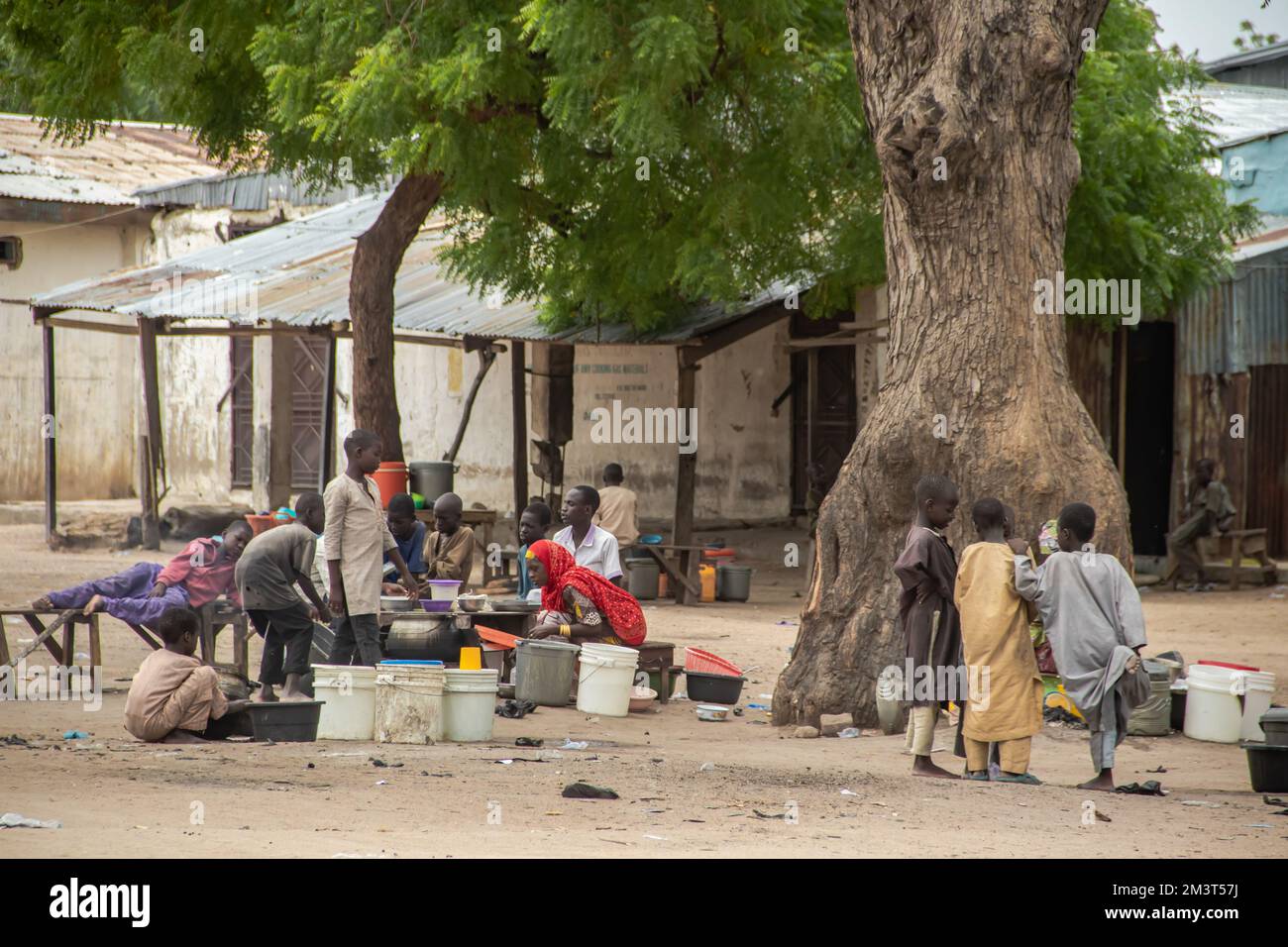 Life Street Fotoszene aus der afrikanischen Straße, Frau, die Essen in einer primitiven Straßenküche verkauft, umgeben von kleinen Kindern, die um sie herum spielen Stockfoto
